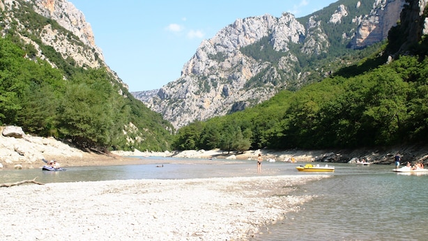 Ein Fluss mit Booten, ein felsiger Berg und grüne Vegetation.