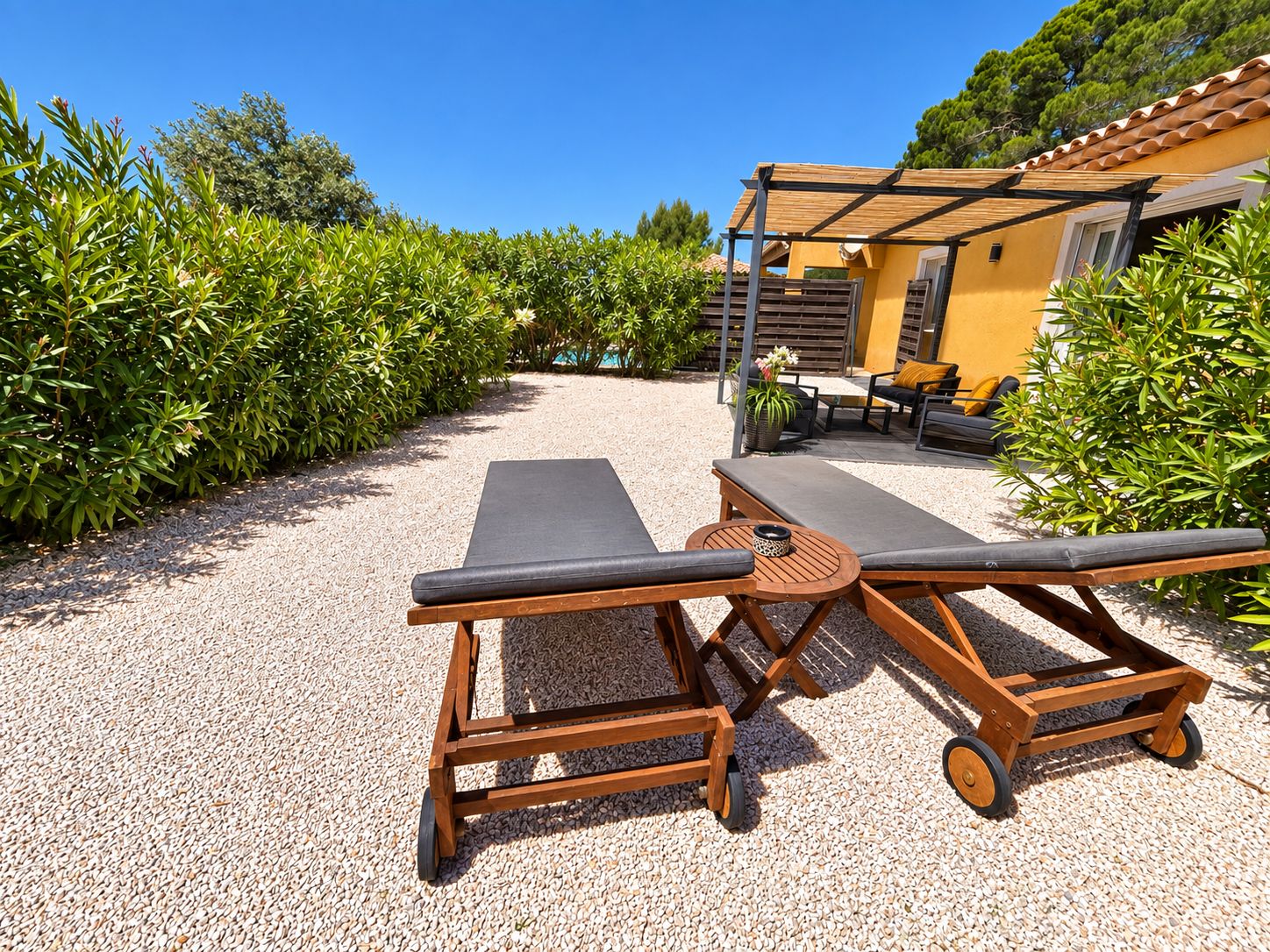 Un espace extérieur ensoleillé, aménagé avec des fauteuils confortables et une petite table, entouré de gravier et de verdure.