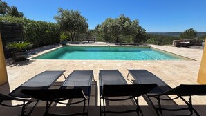 Ein Pool mit Liegestühlen, umgeben von Bäumen und einem klaren Himmel.
