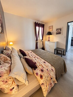 A bedroom with a bed, a bedside table, a lamp, and a view of a hallway.