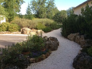 A gravel pathway flanked by rocks and potted plants, leading to a building with a tiled roof.