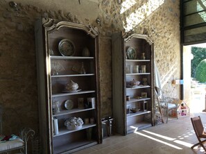 Two ornate wooden bookcases filled with decorative items, a wicker chair, and a view of the outdoors through a window.