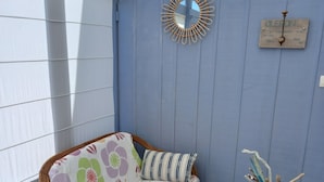 A room with a wicker sofa, patterned cushions, a small wooden table with a glass vase, and a decorative mirror on the wall. - Beautiful house typical from Oleron (Saint-Pierre-D'oléron)