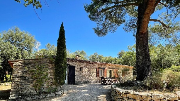 A rustic stone building with a gravel path leading to it, surrounded by trees and vegetation.