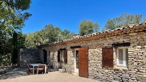 A stone building with a tiled roof, a gravel patio, and a table with chairs.