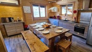 A wooden cabin-style kitchen with a dining table set for four, a refrigerator, and a coffee maker.