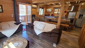 A cozy cabin interior with two sofas, a dining table, and a kitchen area.