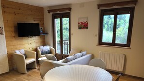 Una habitación acogedora con una mesa redonda, dos sofás y un televisor montado en la pared.