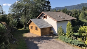 Una casa de dos pisos con entrada de grava y una pequeña construcción de madera al frente.