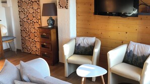 Un salón con un sofá, dos sillones, una mesita blanca, un televisor montado en la pared y una pared de madera con un diseño circular.