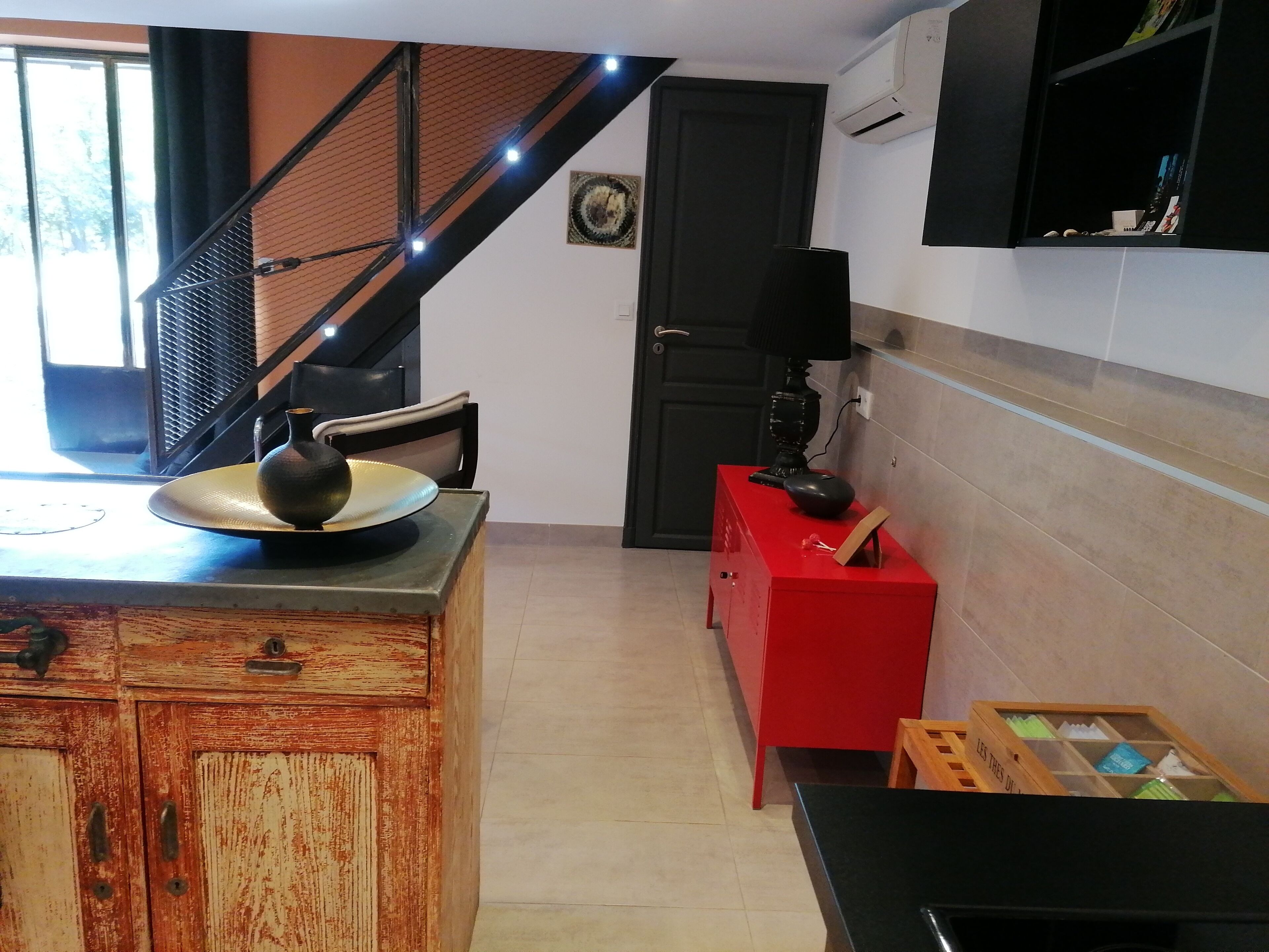 Una cucina con un armadietto in legno rustico, un mobiletto rosso e un tavolo nero con una lampada.