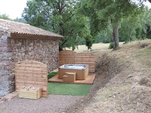 A stone building with a tiled roof, a wooden fence, and a hot tub area with a wooden deck.
