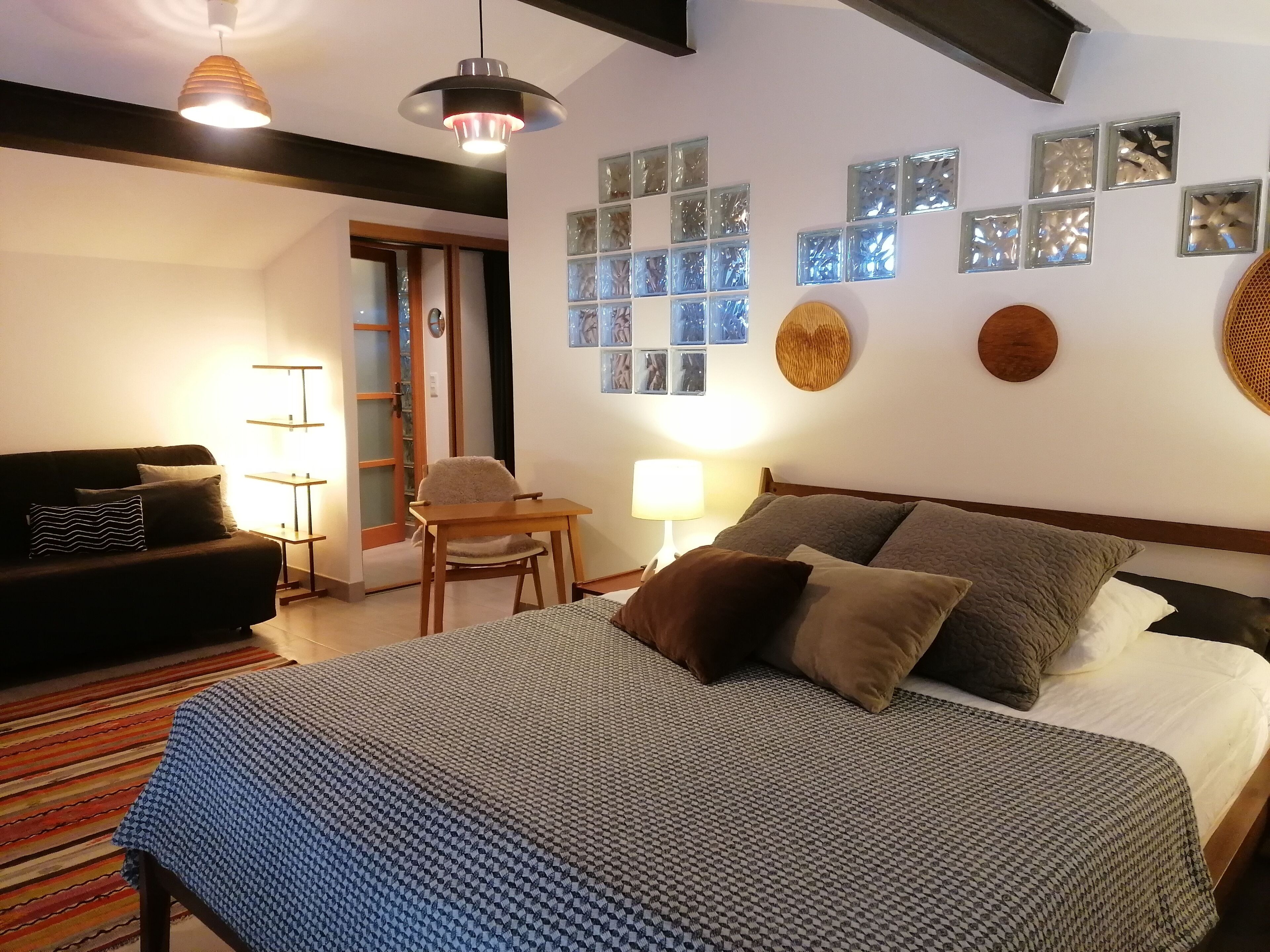 A bedroom with a bed, a desk, a chair, and a sofa. There are wall decorations and a ceiling light.