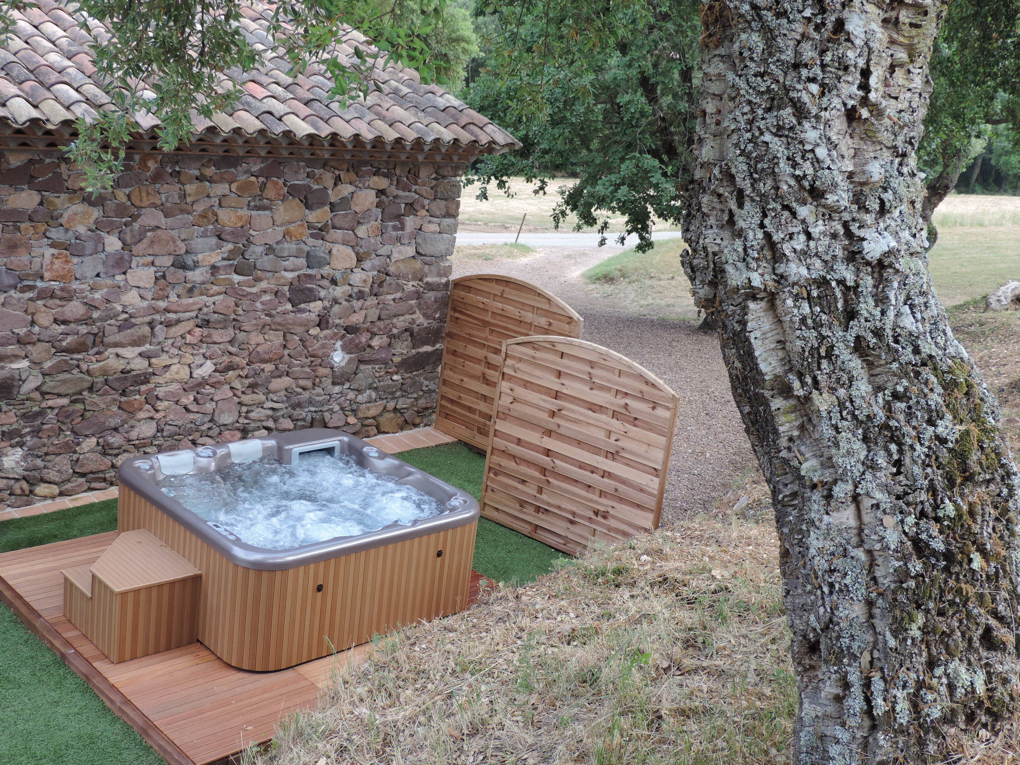 Un edificio de piedra con terraza de madera, un jacuzzi y una verja de madera.