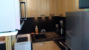A compact kitchen with wooden cabinets, a stainless steel refrigerator, a built-in oven, and a sink.