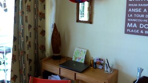 A room with a wooden desk, a laptop, a red chair, a wall-mounted air conditioner, and a sign with text.