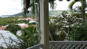 A view from a balcony with a white railing, overlooking a coastal town with red-roofed buildings and lush greenery.