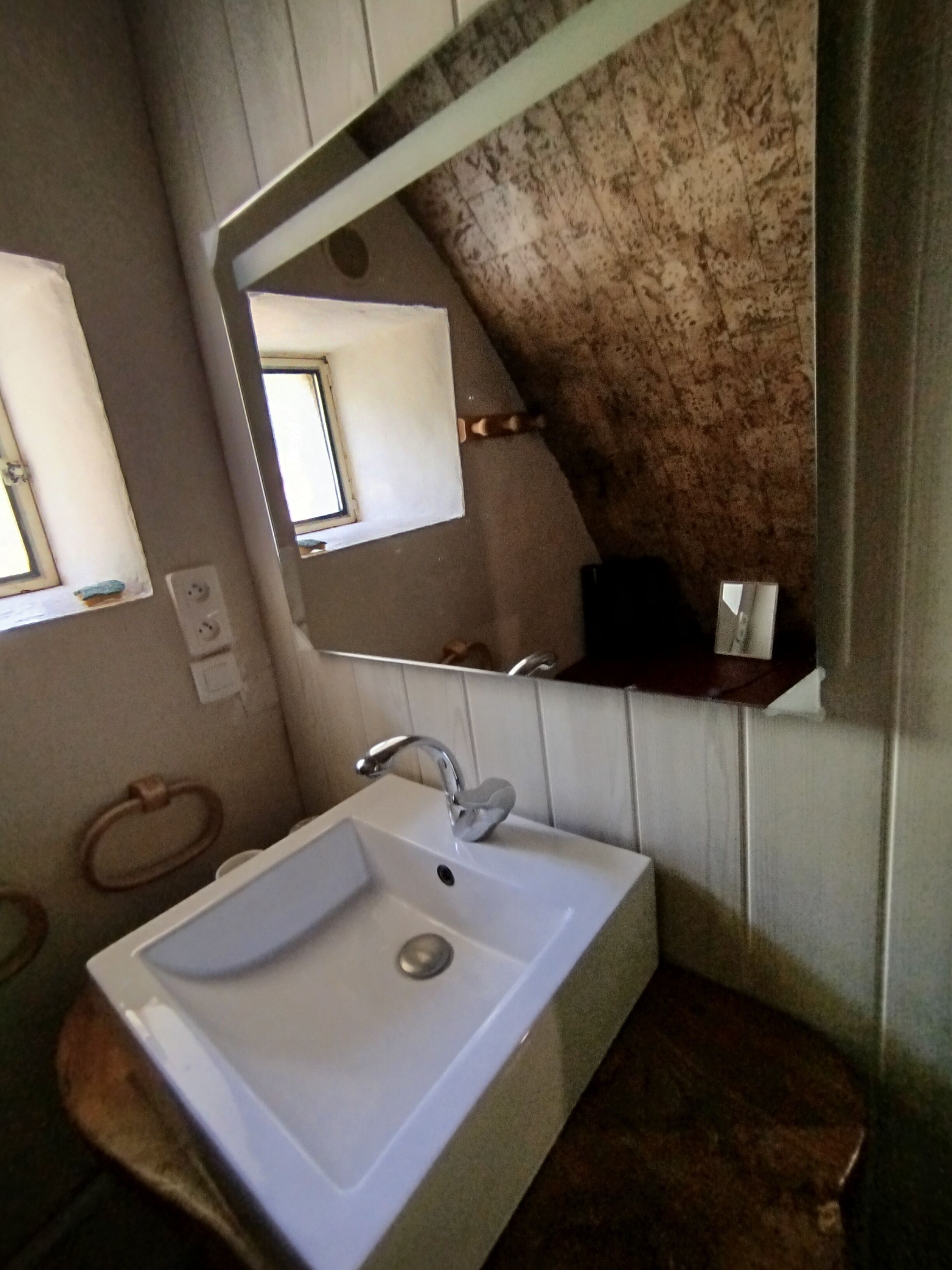 Un baño con lavamanos blanco, un espejo y un perchero para toallas.