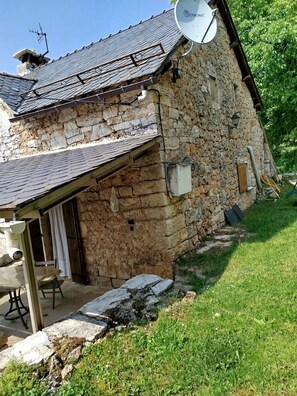 A stone house with a sloped roof, a satellite dish, and a small outdoor seating area. - Restored farmhouse in its original style. Accommodation in Caussignac. (ST ENIMIE)