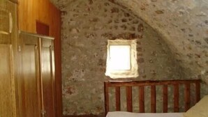 Een slaapkamer met een stenen muur, een houten bed en een raam.
