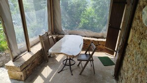 Een overdekt terras met een tafel en stoelen, stenen muren en uitzicht op groen.