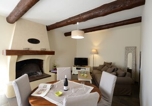 Ein gemütliches Wohnzimmer mit Kamin, einem Esstisch für zwei Personen, einer Couch und einem Fernseher.