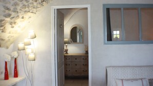 A room with a stone ceiling, a wooden dresser with drawers, a mirror above the dresser, and a window with a blue frame.
