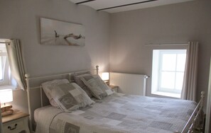 A bedroom with a bed, a nightstand, a window, and a radiator.