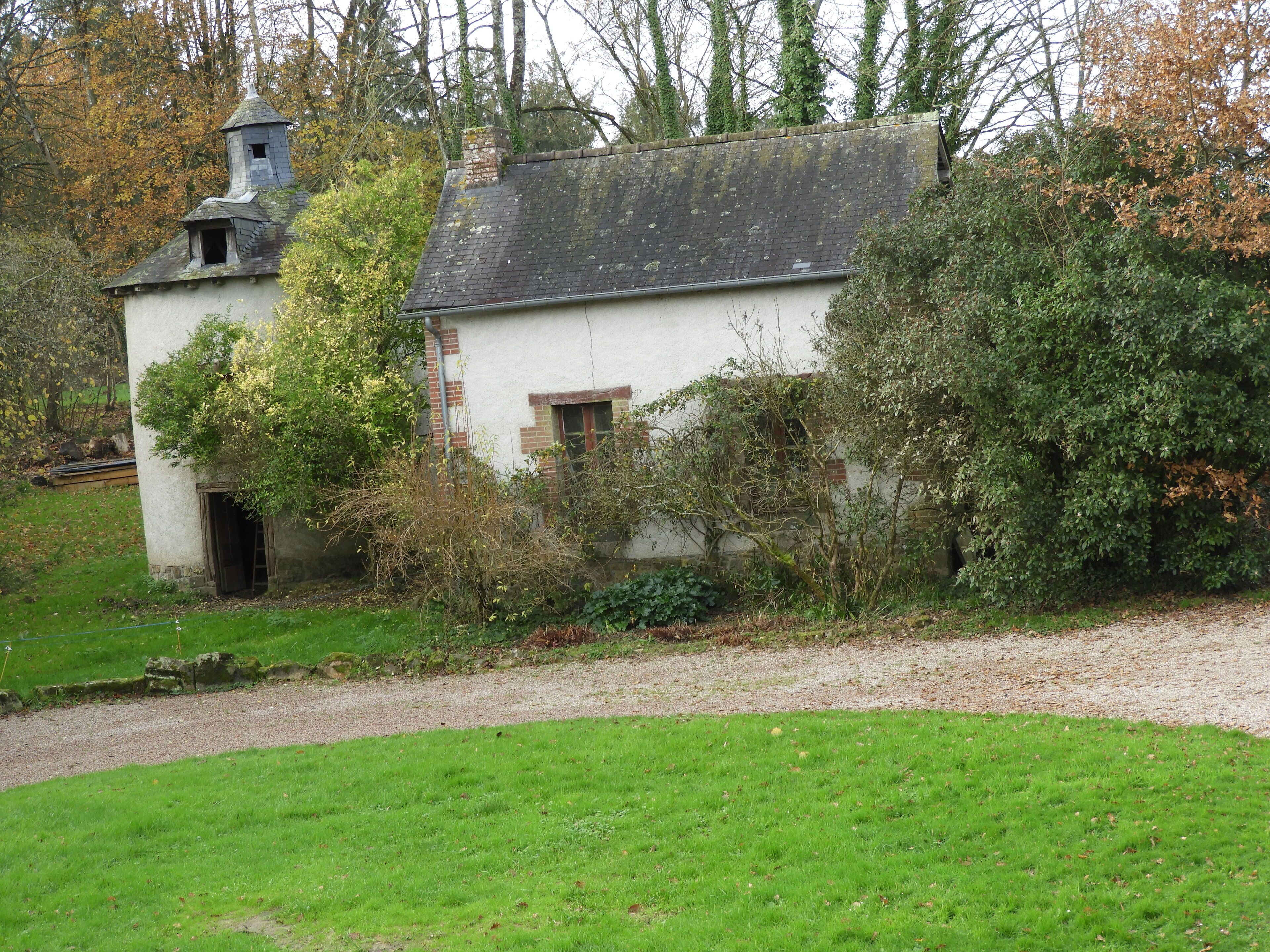Un petit bâtiment rustique doté d’une cheminée, entouré d’une végétation luxuriante et d’arbres.