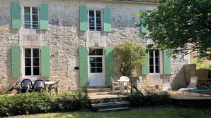 A stone building with green shutters, a white door, and a small porch with outdoor seating. - Witihin the marais poitevin, house with character is an enjoyable place to stay (Damvix)