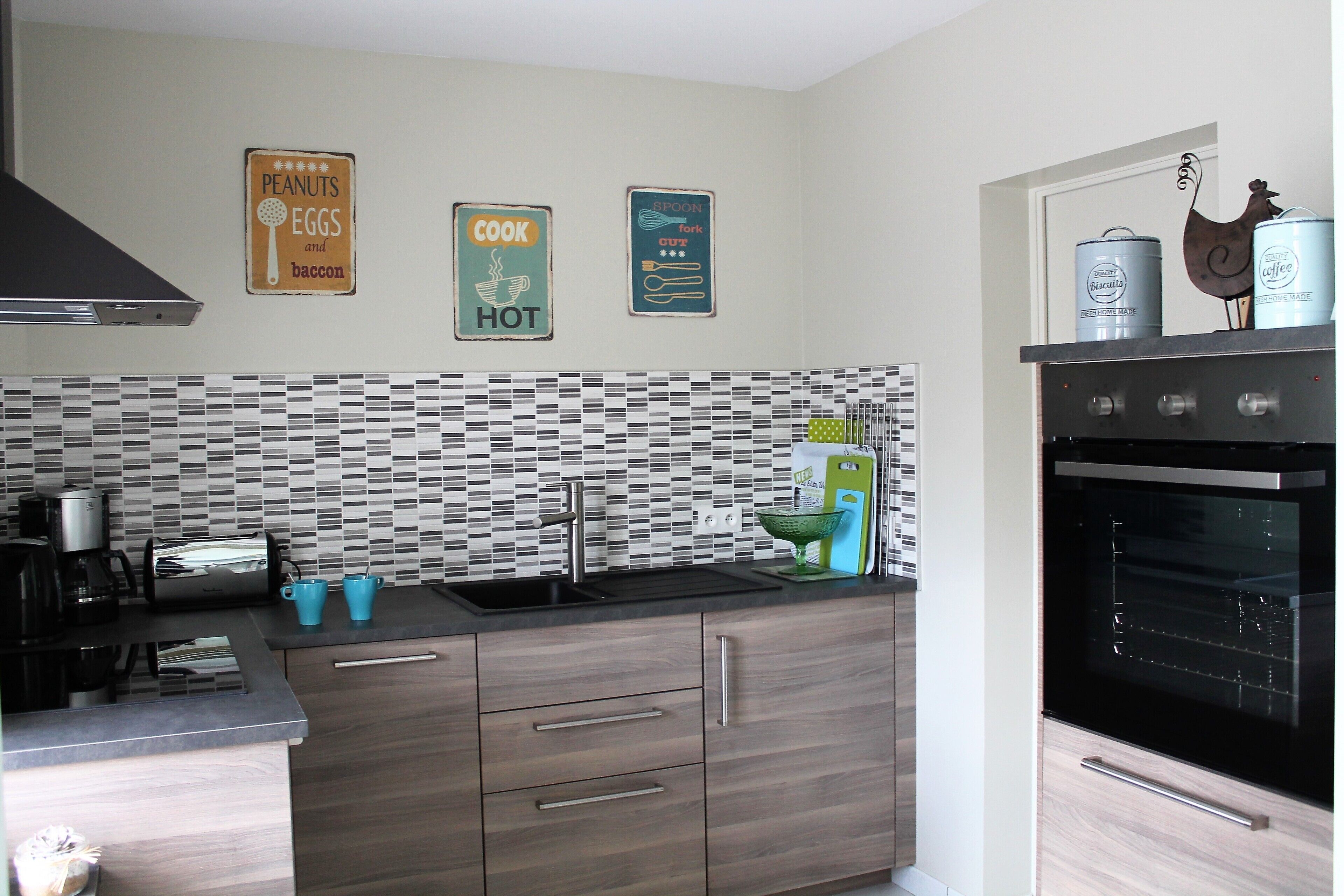 Una cocina moderna con estufa negra, un fregadero y salpicadero de azulejos. Hay tres letreros en la pared con frases relacionadas con la cocina.