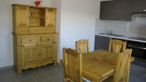 Een keuken met houten kastjes, een eettafel met stoelen en een inbouwoven.