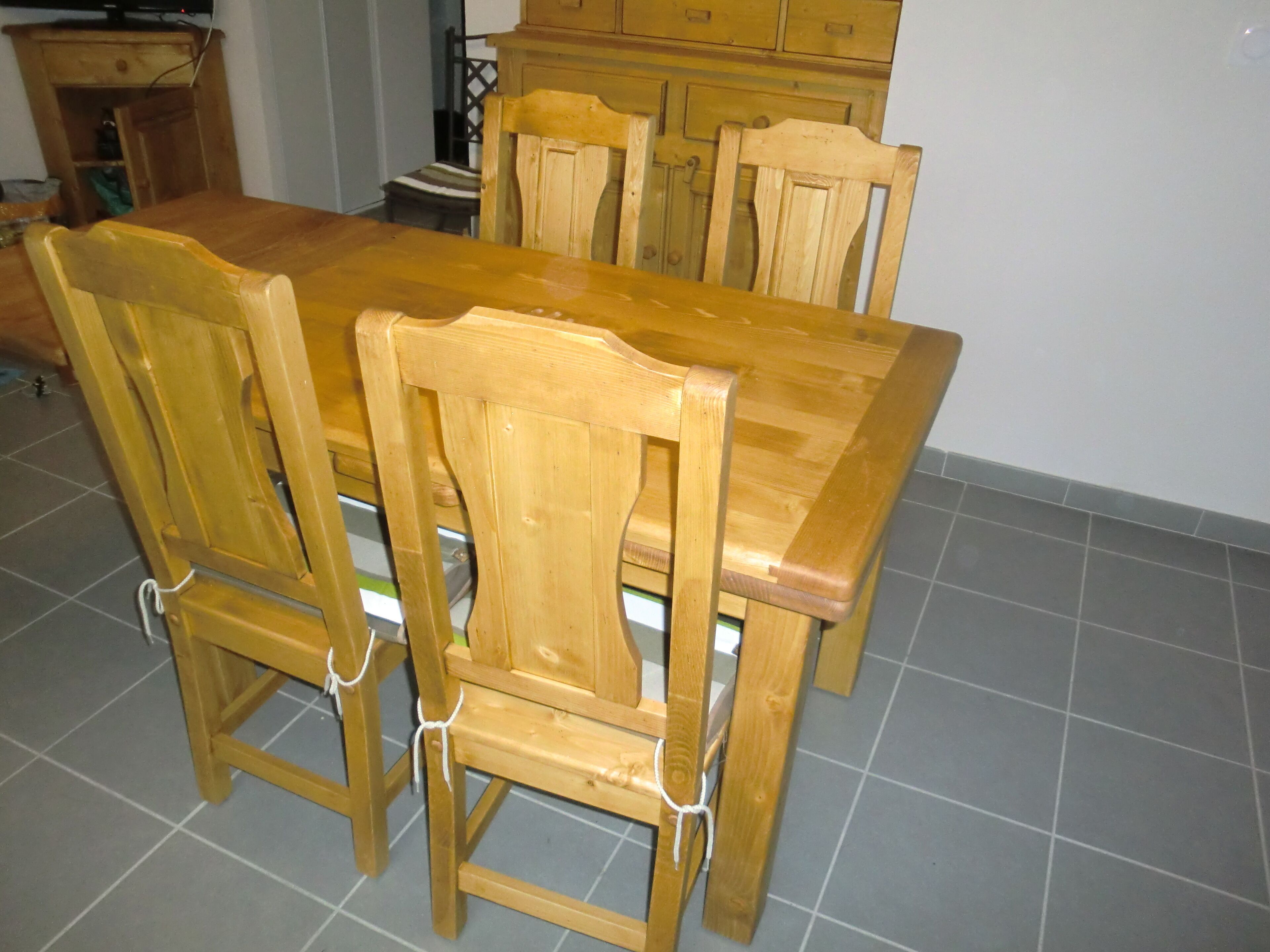 Una mesa de comedor de madera con cuatro sillas, suelo de baldosas y armarios de madera al fondo.
