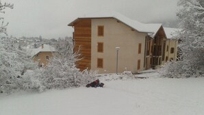 Een gebouw met een houten gevel en meerdere ramen, omgeven door met sneeuw bedekte begroeiing.