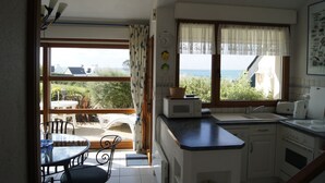Una cocina con vista al mar, un comedor con mesa y sillas, y un ventanal con cortinas.