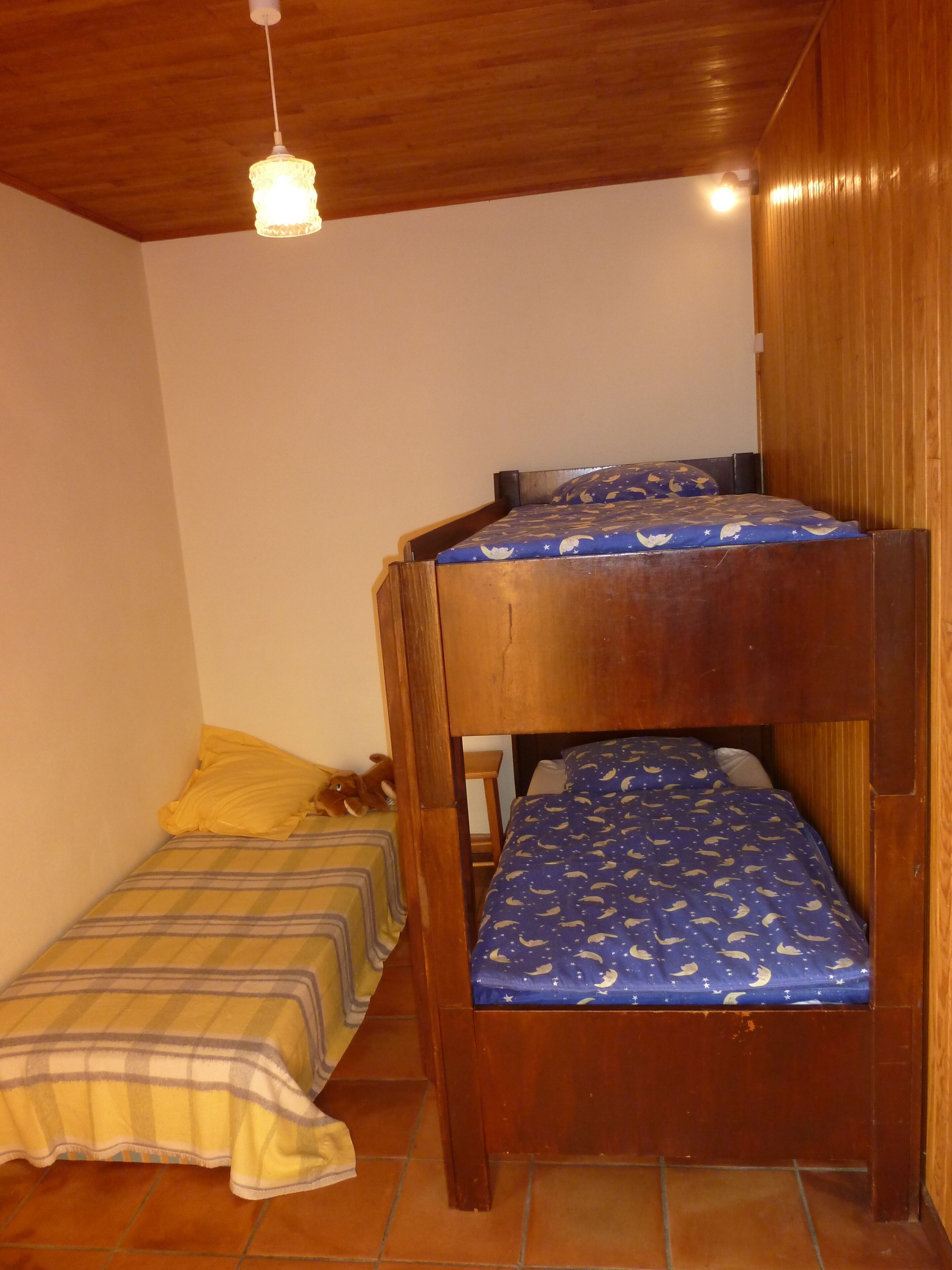 Habitació petita i acollidora amb una llitereta superposada i un llit individual. Té sostre de fusta i una làmpada penjant.