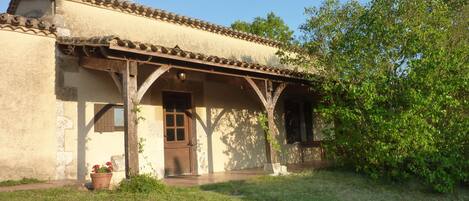A rustic building with a tiled roof, a wooden porch, and a small garden area.