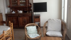 Una habitación con una mesa de comedor, sillas de mimbre, una pequeña mesa de madera, un televisor y un armario.