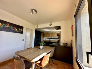 Un comedor con una mesa de madera y dos sillas, una cocina al fondo y una ventana con vistas.