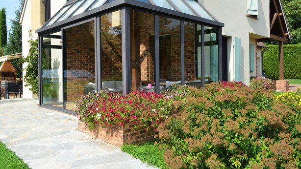 A conservatory with a glass roof, brick walls, and a garden with various flowers.
