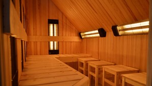 A sauna room with wooden benches and tables, wooden walls, and two infrared heaters.