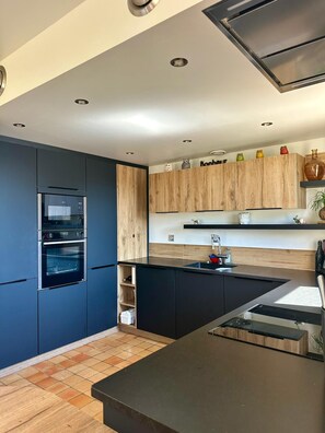 Une cuisine moderne dotée d’appareils électroménagers intégrés, d’un pare-feu en bois et d’un plan de travail noir.