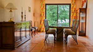 A dining area with a table and chairs, a cabinet with drawers, a lamp, and a window with curtains.