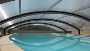 An indoor swimming pool with a curved design, surrounded by a glass enclosure and a stone deck.