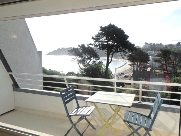 Een balkon met een tafel en twee stoelen, met uitzicht op een strand en een kustplaats.
