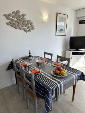 Un coin repas avec une nappe à rayures, des chaises, un saladier, des assiettes et des fruits.