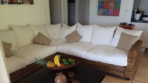 Un salon avec un canapé blanc, une table basse noire et un panier de fruits.