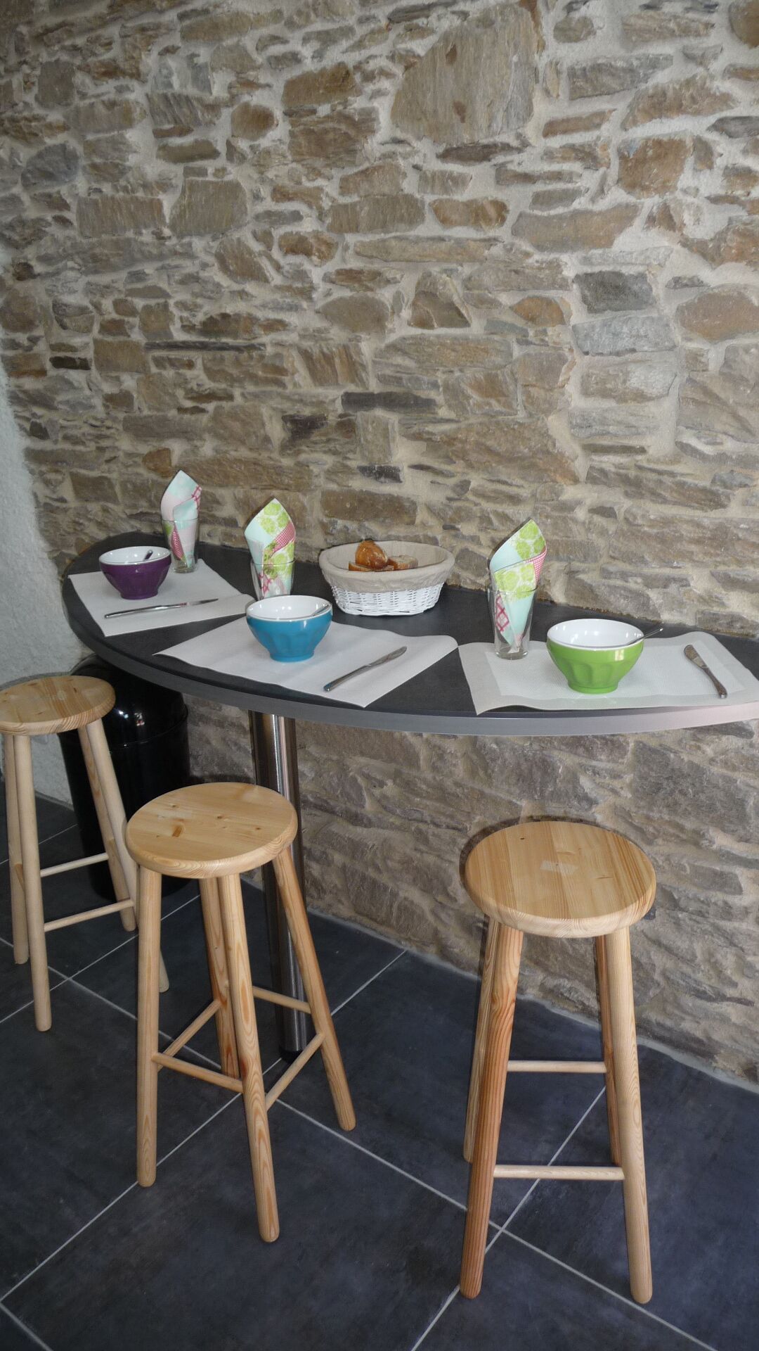 Un mur de pierres avec une table dressée pour un repas, agrémentée de différents bols et d’un panier.