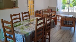 Een eetruimte met een tafel gedekt voor vier personen, houten stoelen, een hanglamp, een deur met raam en uitzicht op groen buiten.