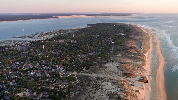 Luchtbeeld van een kustplaatsje met een strand, huizen en een vuurtoren.